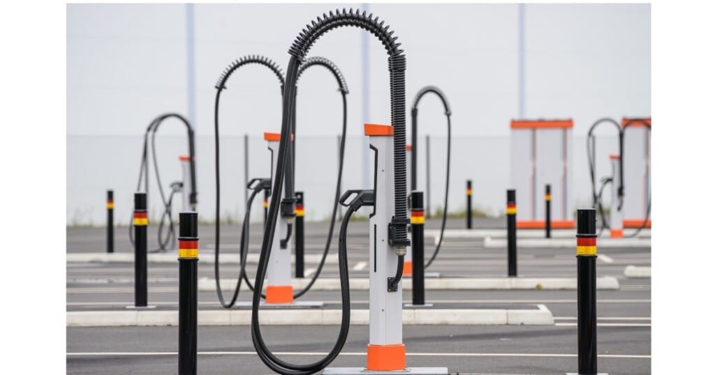 Empty electric vehicle charging stations with tall, flexible cables stand in a lined-up pattern in a parking lot.