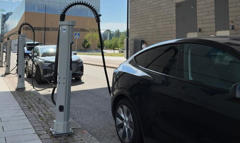 Several electric cars are parked in a row and charging at modern charging stations on a city street during the day.